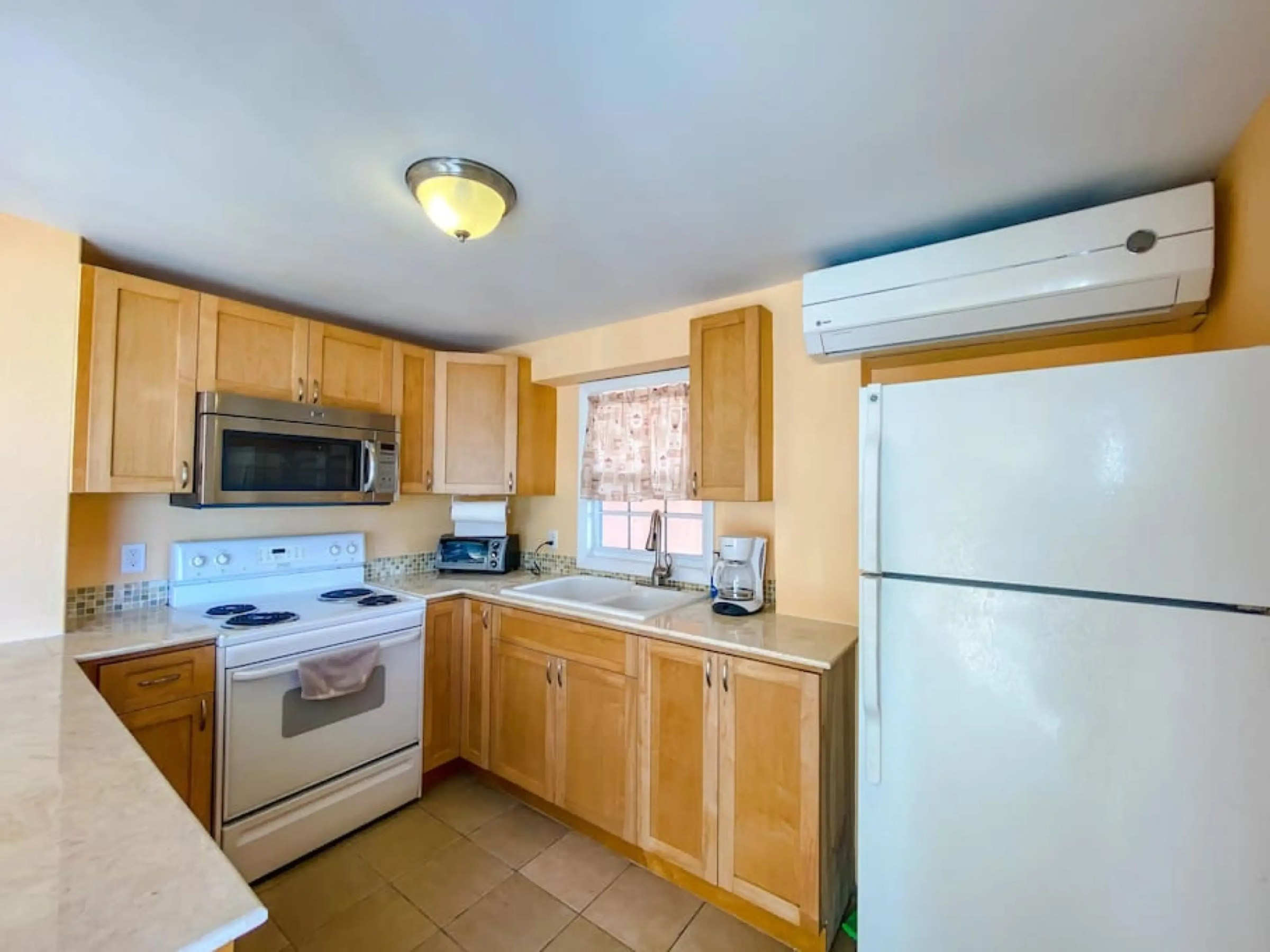 Small kitchen with wooden cabinets, stove, microwave, fridge, and sink under a window.