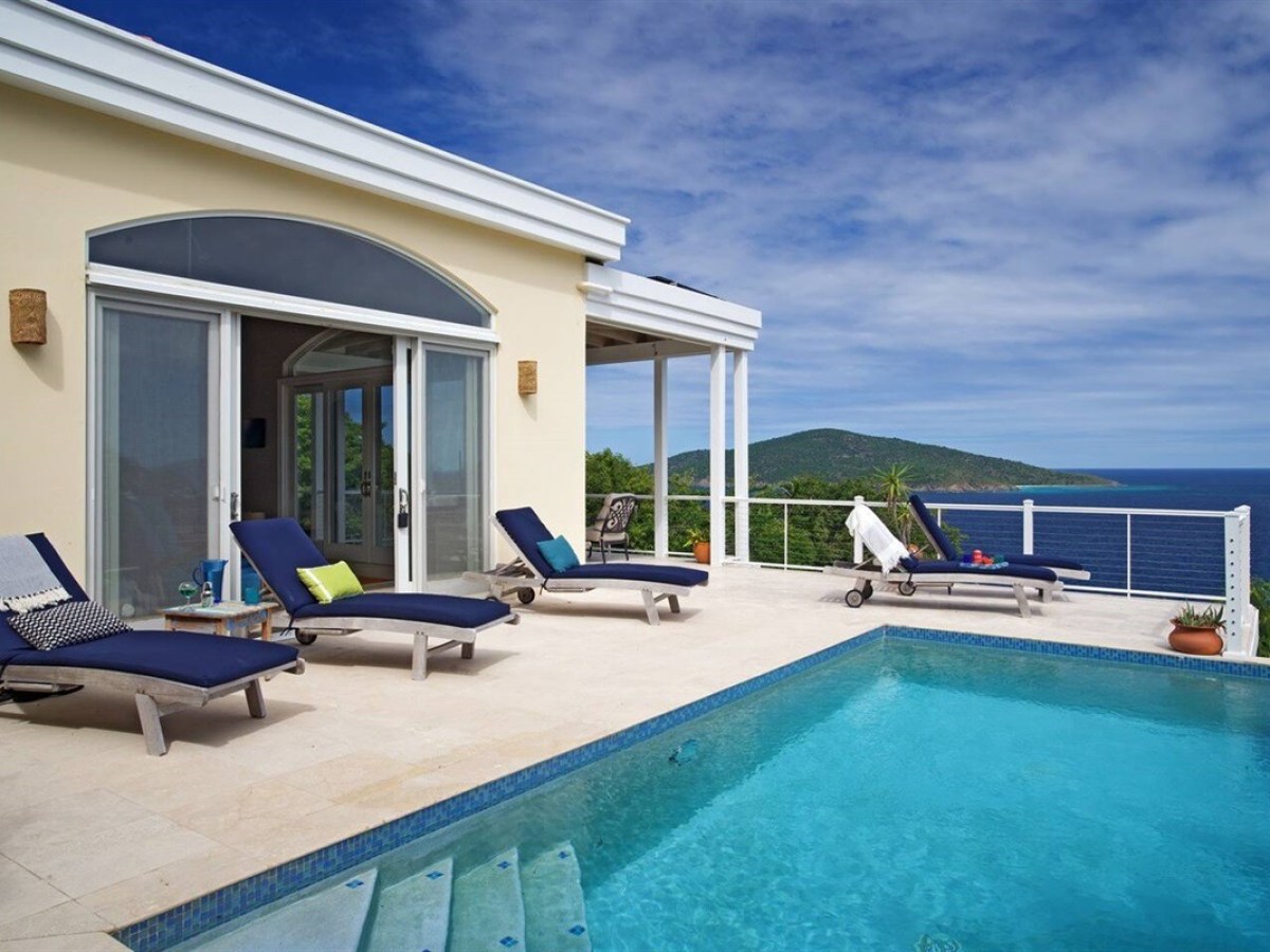 Ocean view patio with pool, lounge chairs, and a modern house.