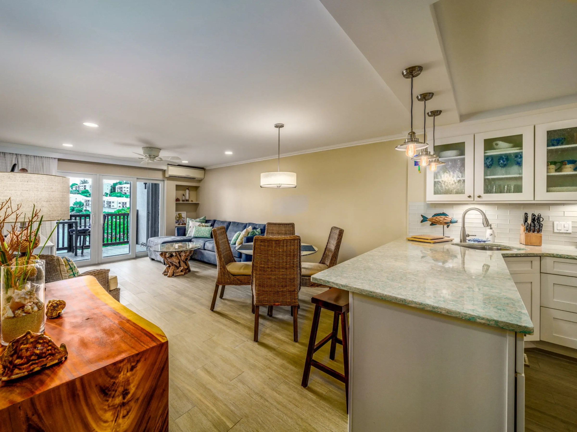 Open living area with kitchen, sofa, dining table, and balcony; modern decor with wooden furniture and lighting.