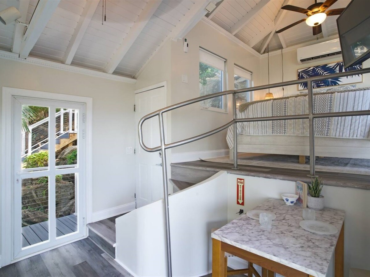 Cozy loft with bed, dining table, stairs, and large window with garden view.
