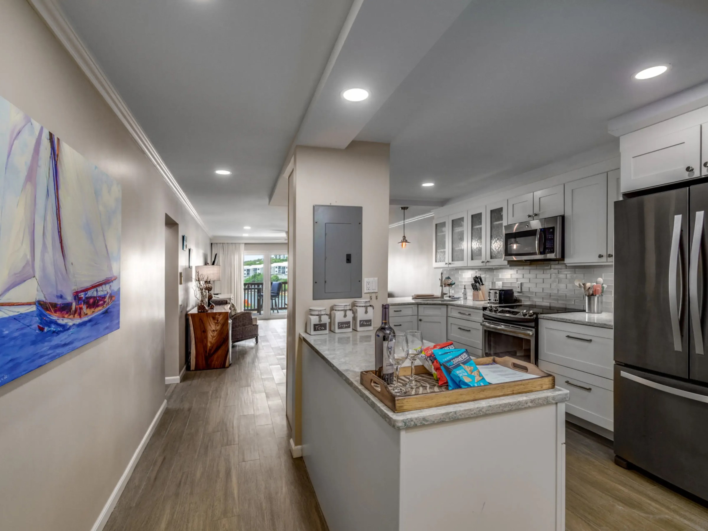 Modern kitchen and hallway with white cabinets and wood flooring.