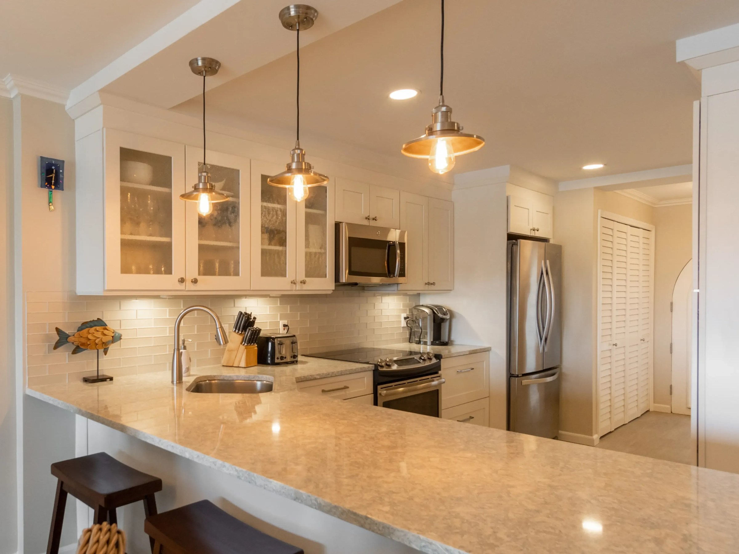 Modern kitchen with pendant lights, stainless steel appliances, and light countertops.