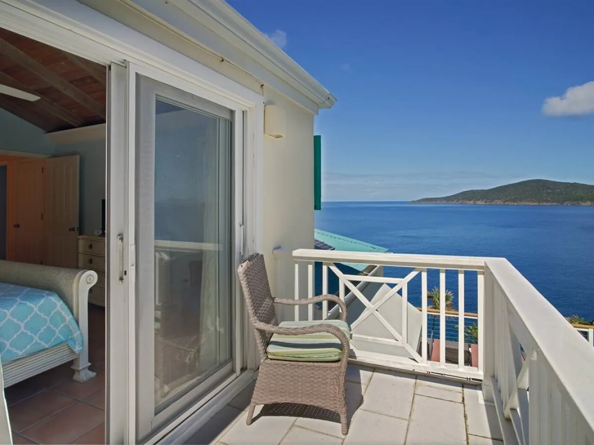 Bedroom with open sliding doors leading to a terrace overlooking the sea and distant island.
