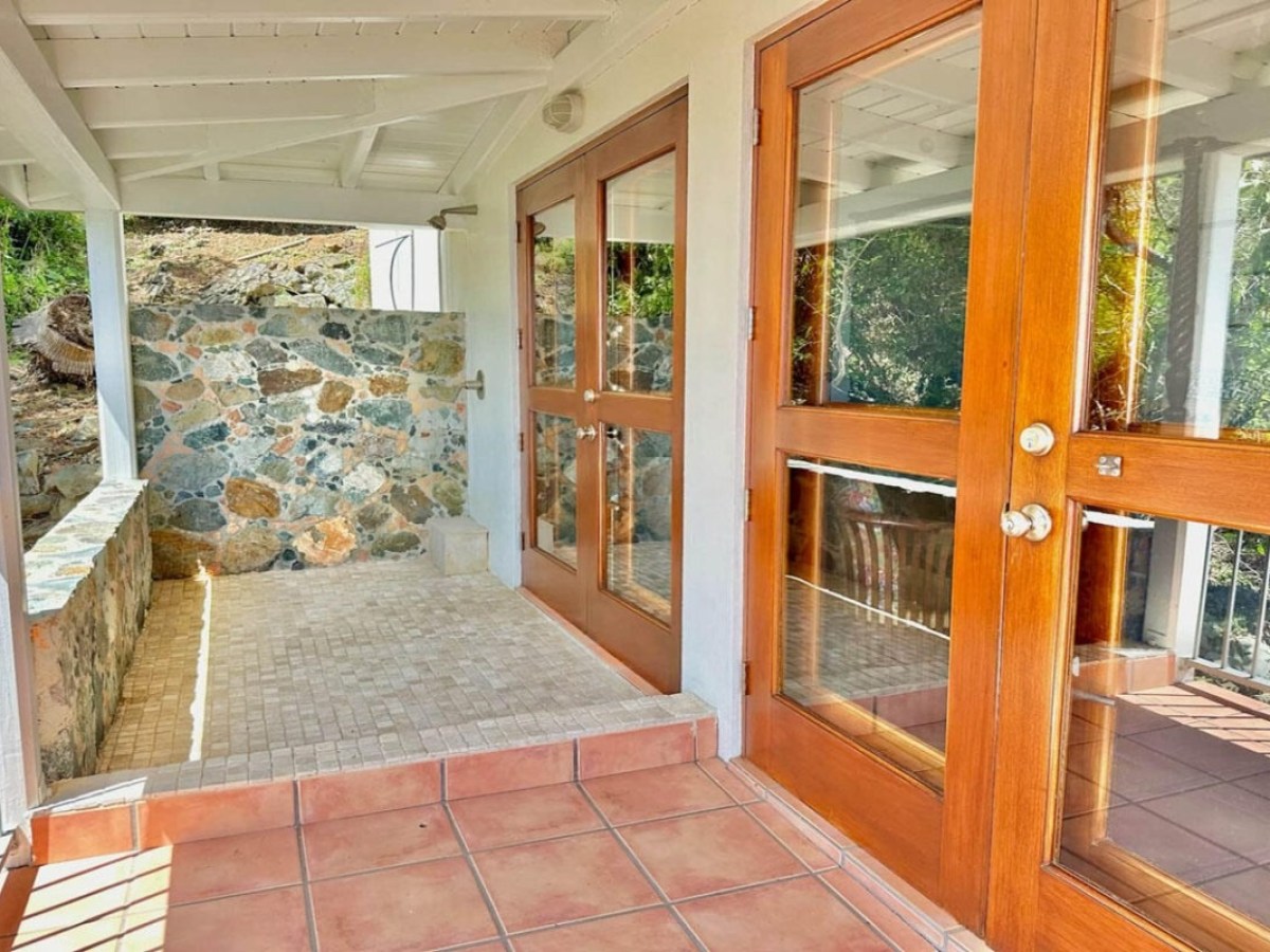 Covered porch with tile floor, wooden doors, and stone wall, partly enclosed by glass.