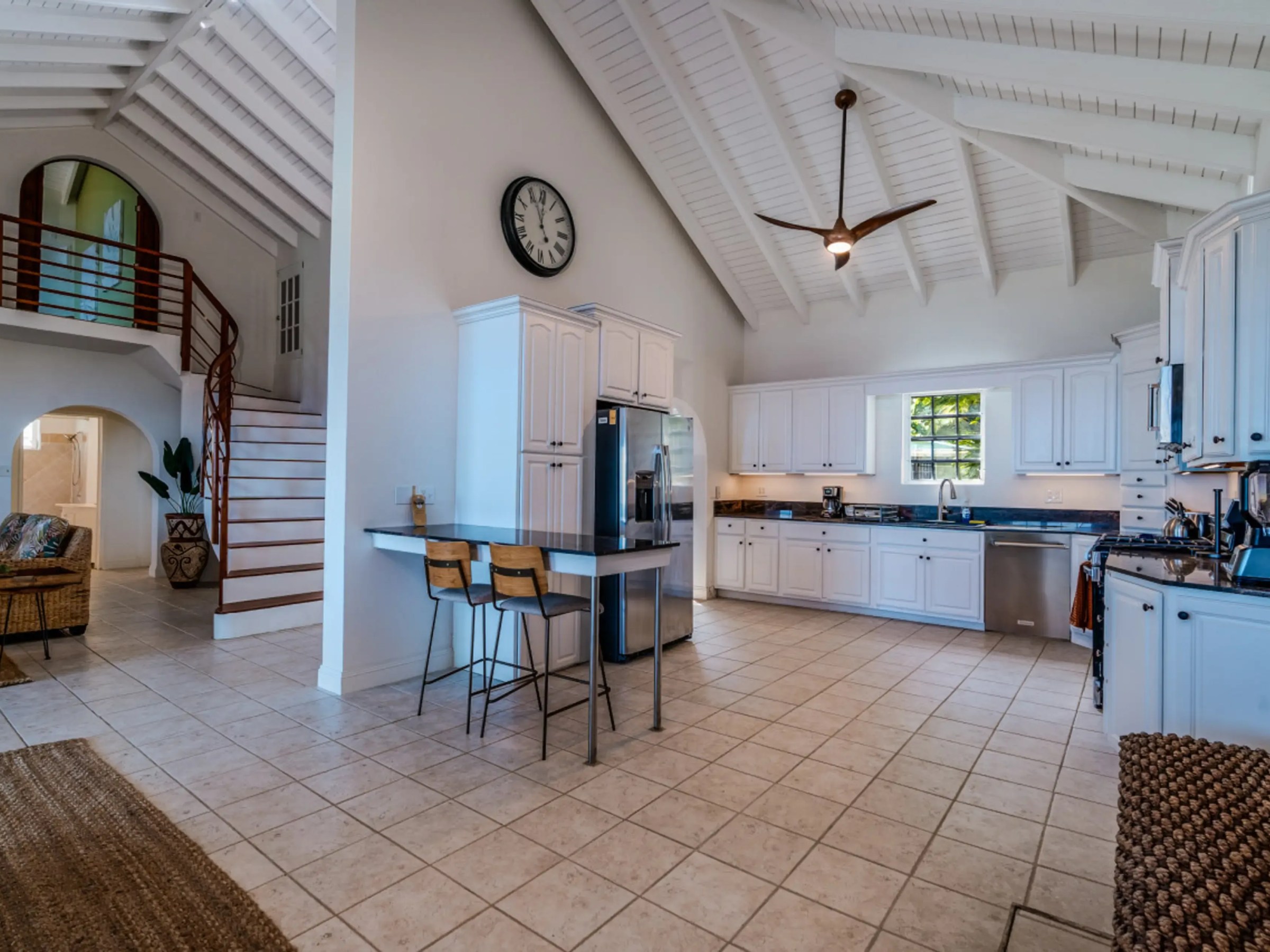 Spacious kitchen with vaulted ceiling, white cabinets, and bar stools at island.