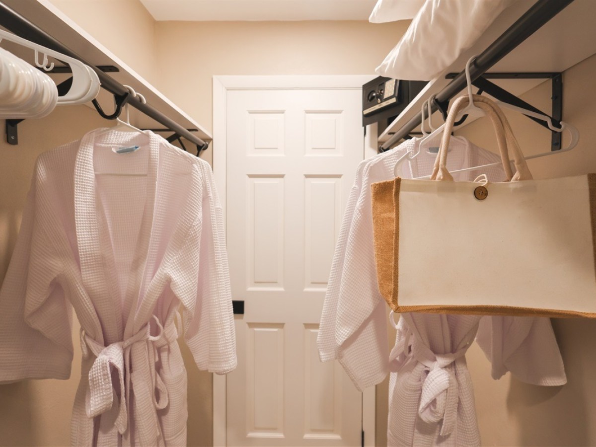 Two white bathrobes and a canvas tote bag in a closet with hangers.