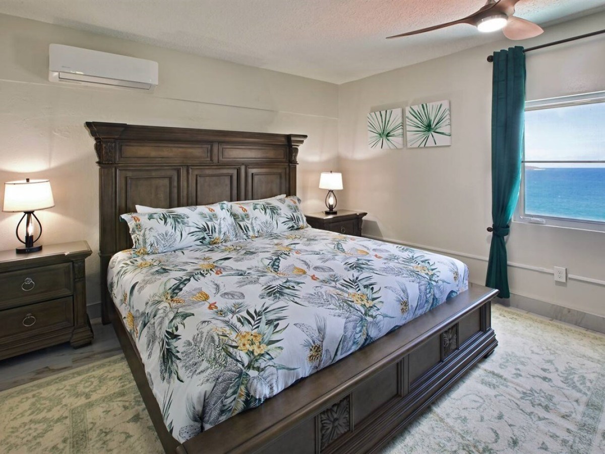 Bedroom with wooden bed, floral bedding, two nightstands, and ocean view from window.