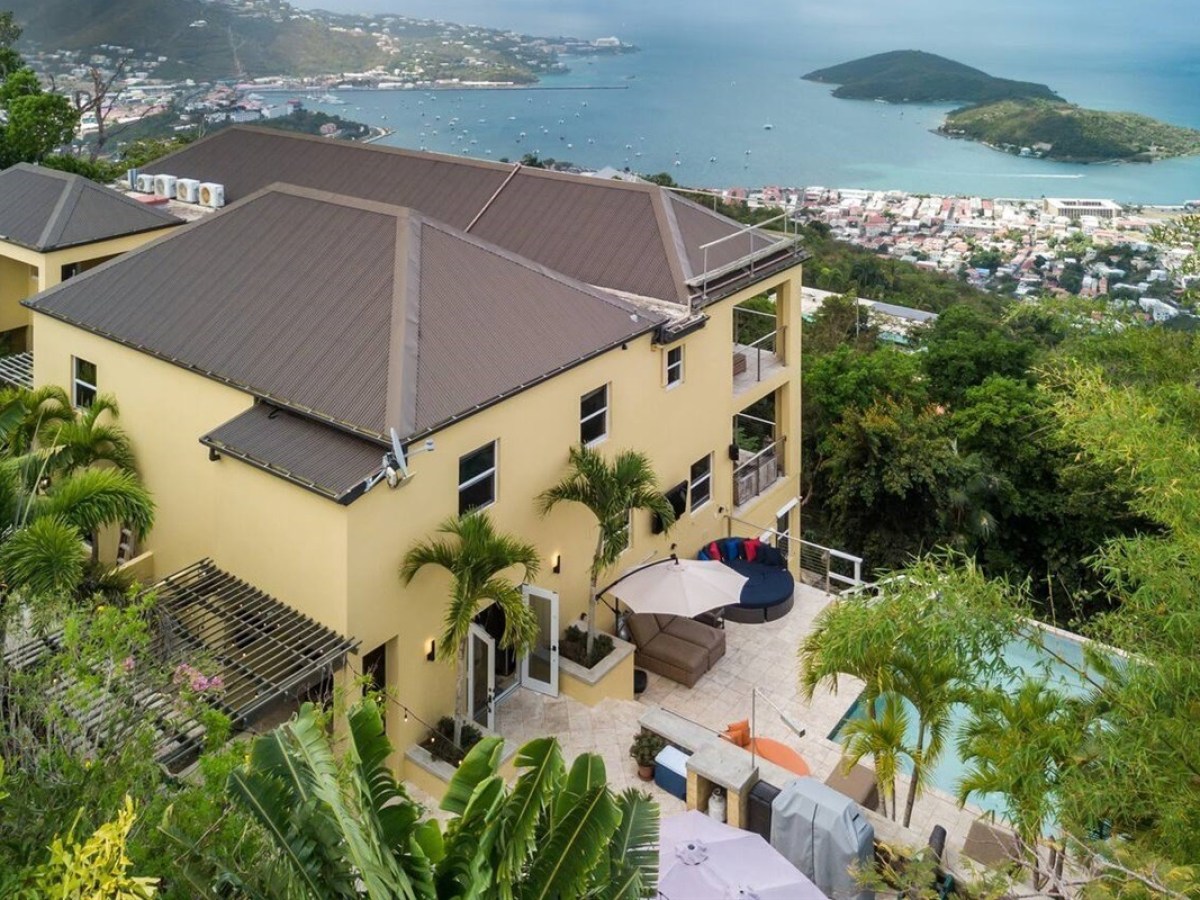 Hilltop villa with a pool and ocean view, surrounded by lush greenery.