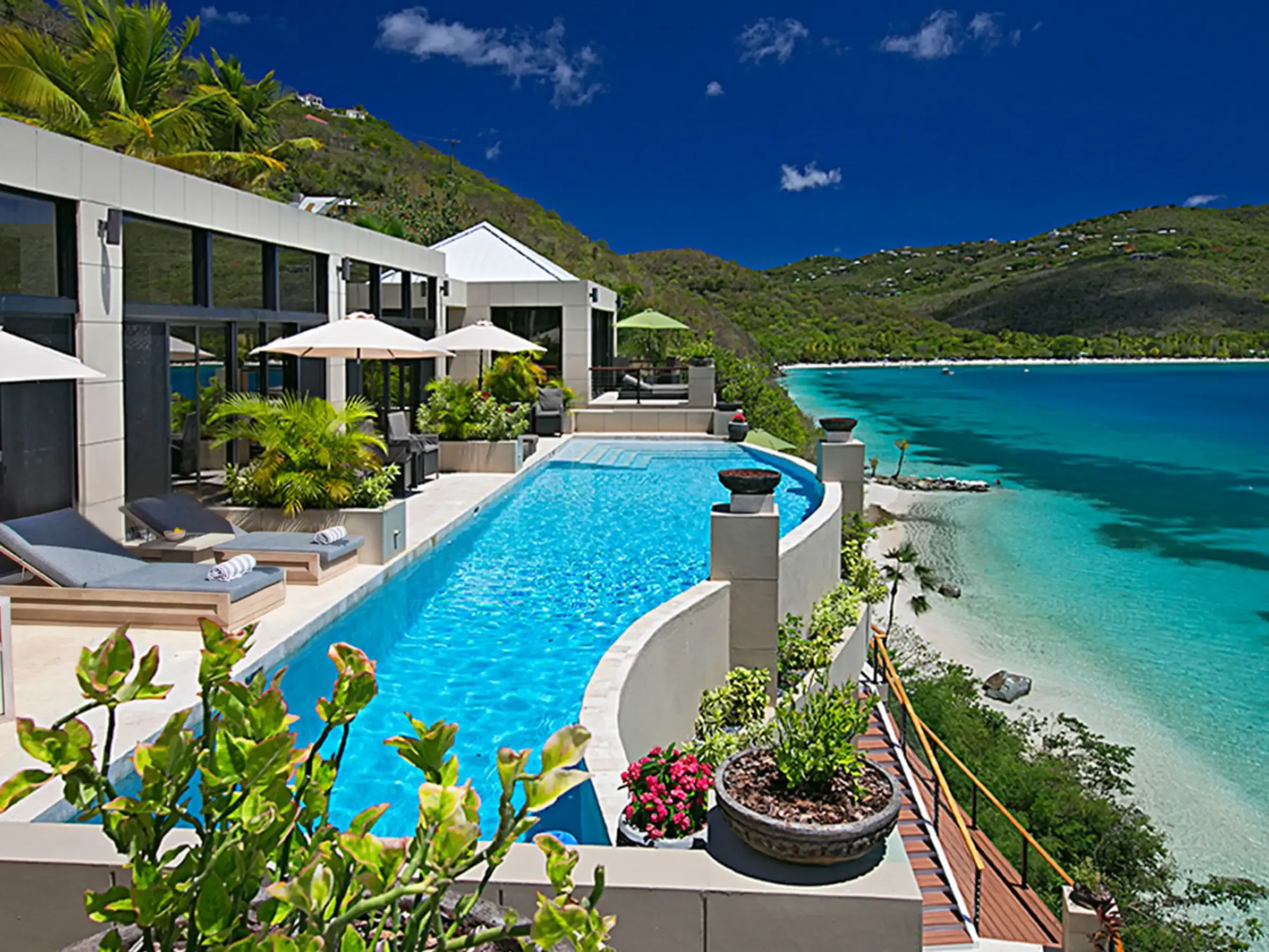 Luxury villa with an infinity pool overlooking a turquoise ocean and lush hillside.