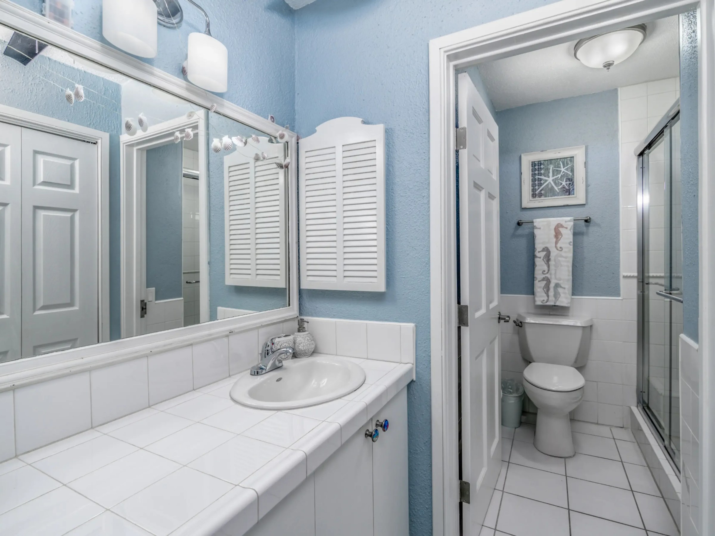 Blue and white bathroom with a mirror, sink, toilet, and shower.