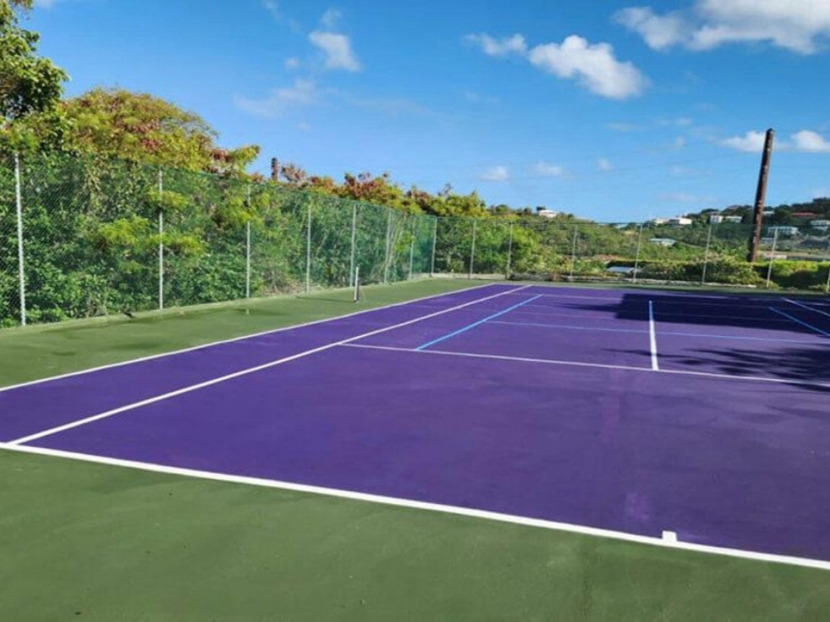Outdoor tennis court with purple surface and green surroundings under a blue sky.