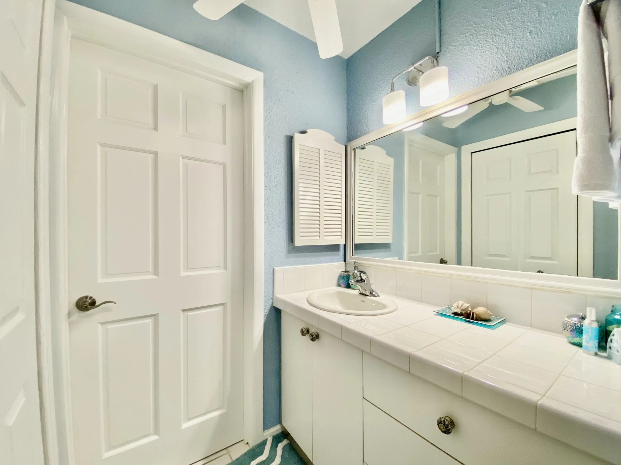 Small bathroom with white cabinets, large mirror, blue walls, and a decorative counter.