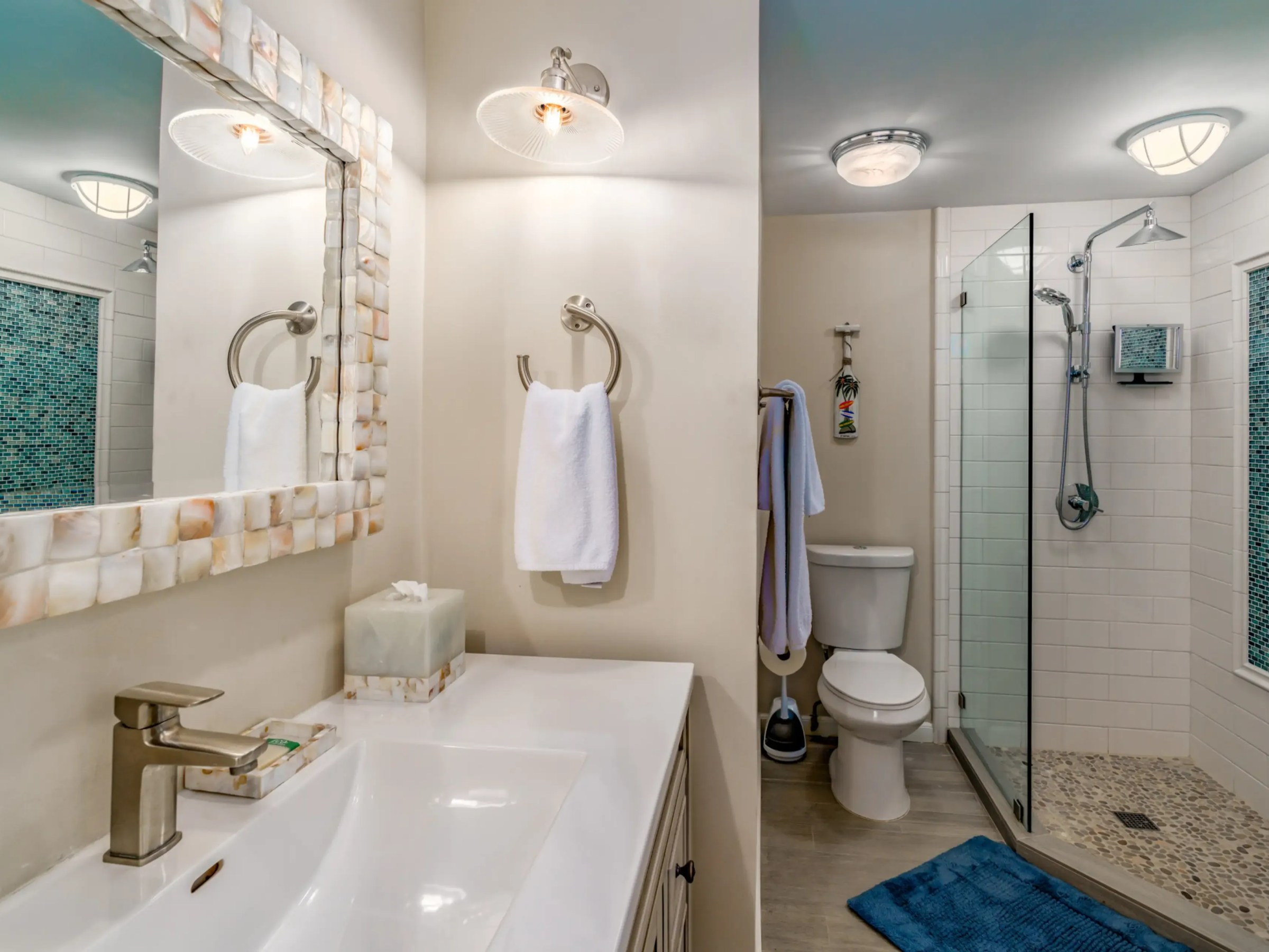 Modern bathroom with a glass shower, toilet, and marble-countered sink with a large mirror.