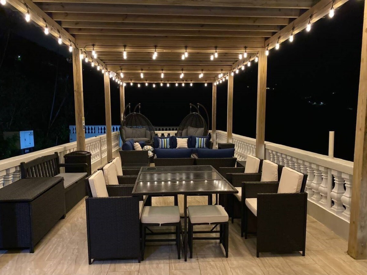 Outdoor patio at night with string lights, rattan furniture, and hanging chairs under a wooden pergola.
