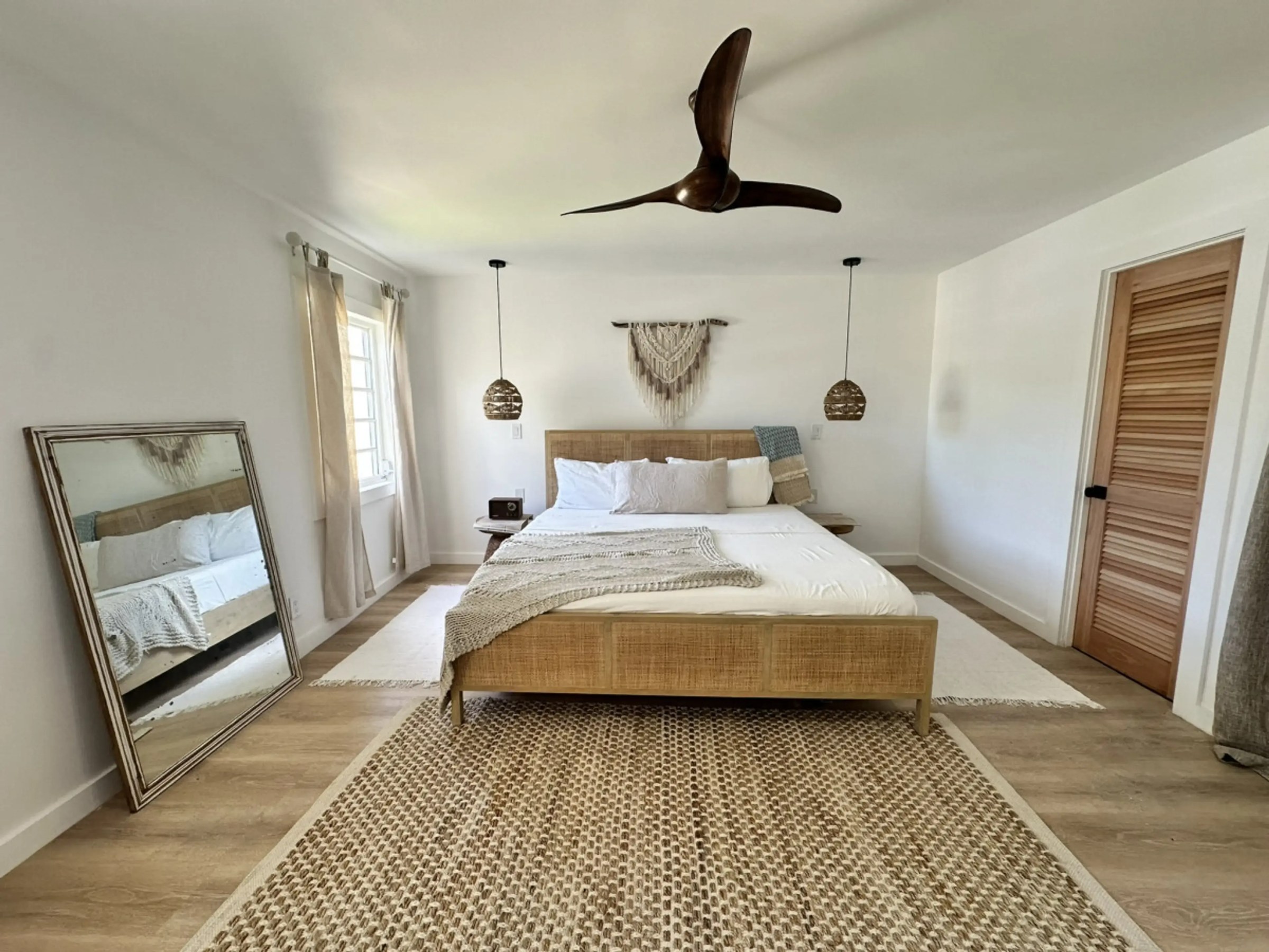 Modern bedroom with wooden bed, beige rug, and large mirror.
