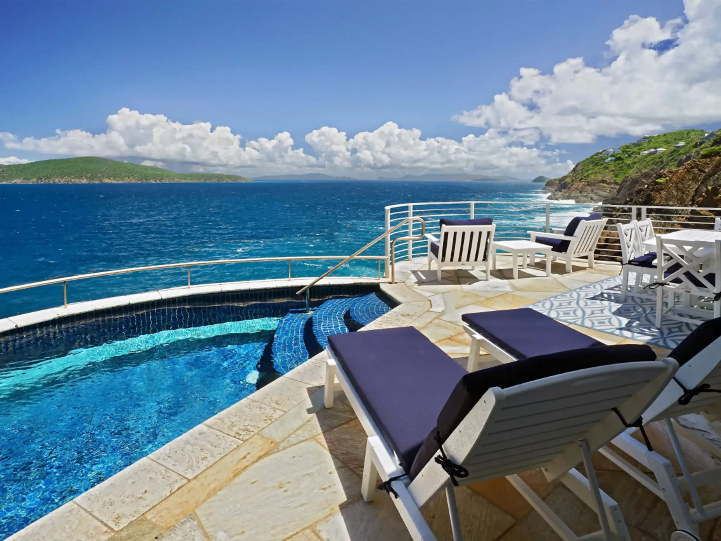 Luxury poolside overlooking ocean with lounge chairs and dining set.