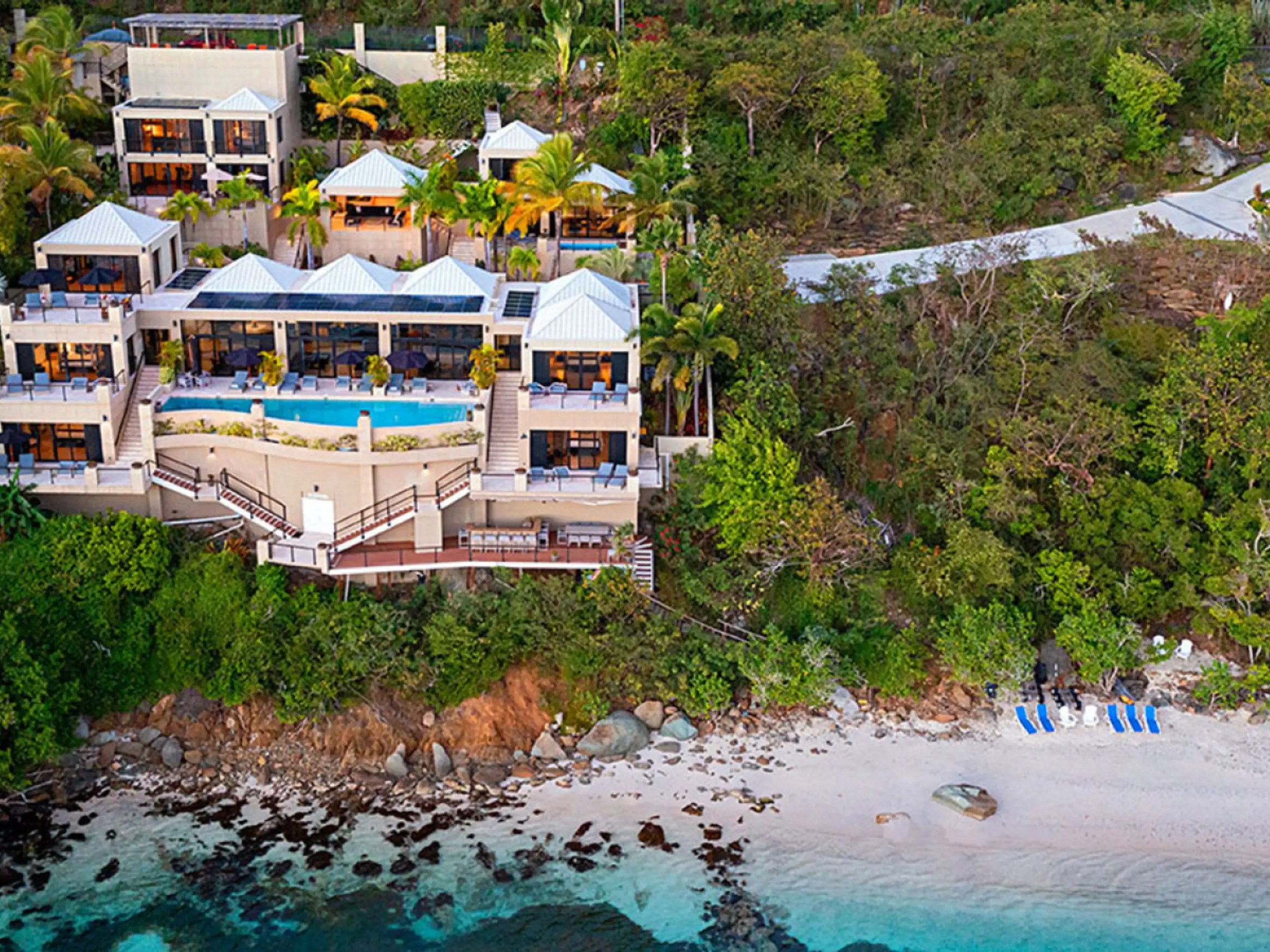 Aerial view of a luxurious beachside villa surrounded by trees and a sandy shore.