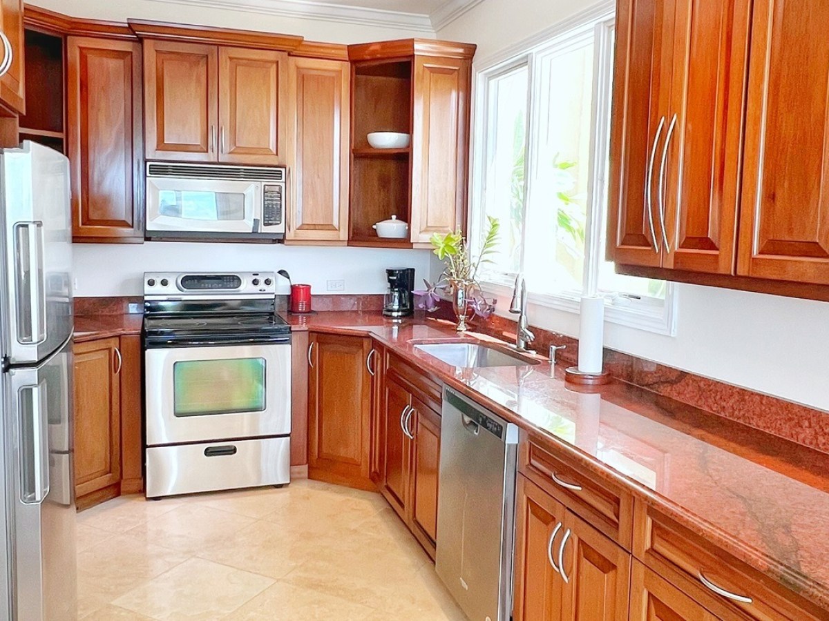 Modern kitchen with wooden cabinets, stainless steel appliances, and red countertops.
