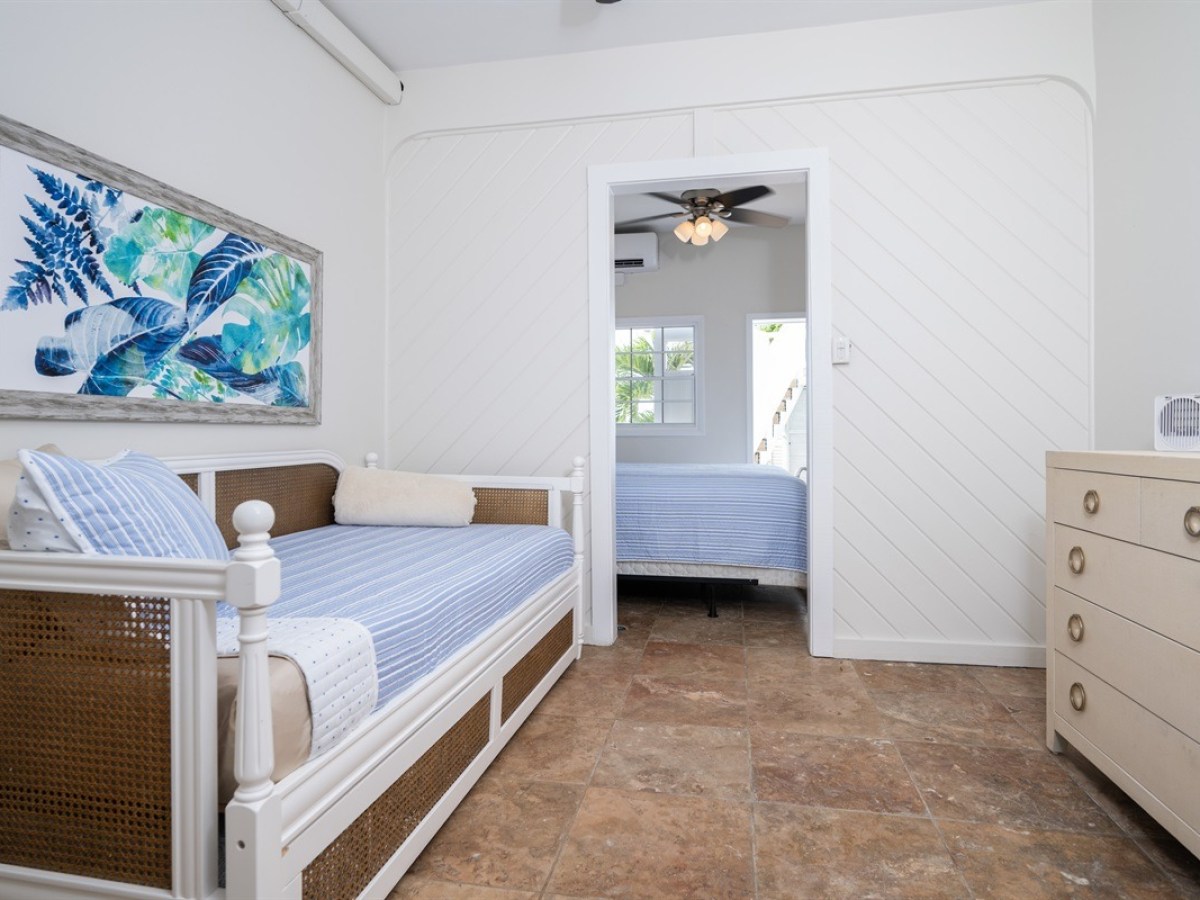 Bedroom with daybed, tropical wall art, dresser, and view into another room with bed.