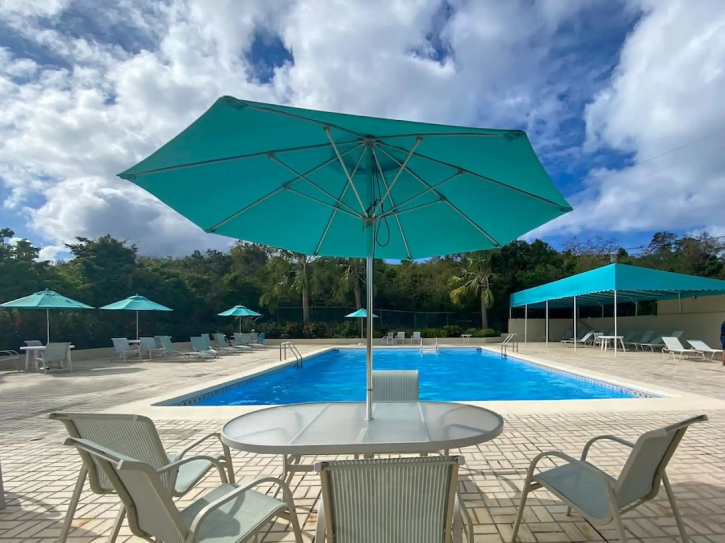 Outdoor pool area with turquoise umbrellas, chairs, and cloudy sky.