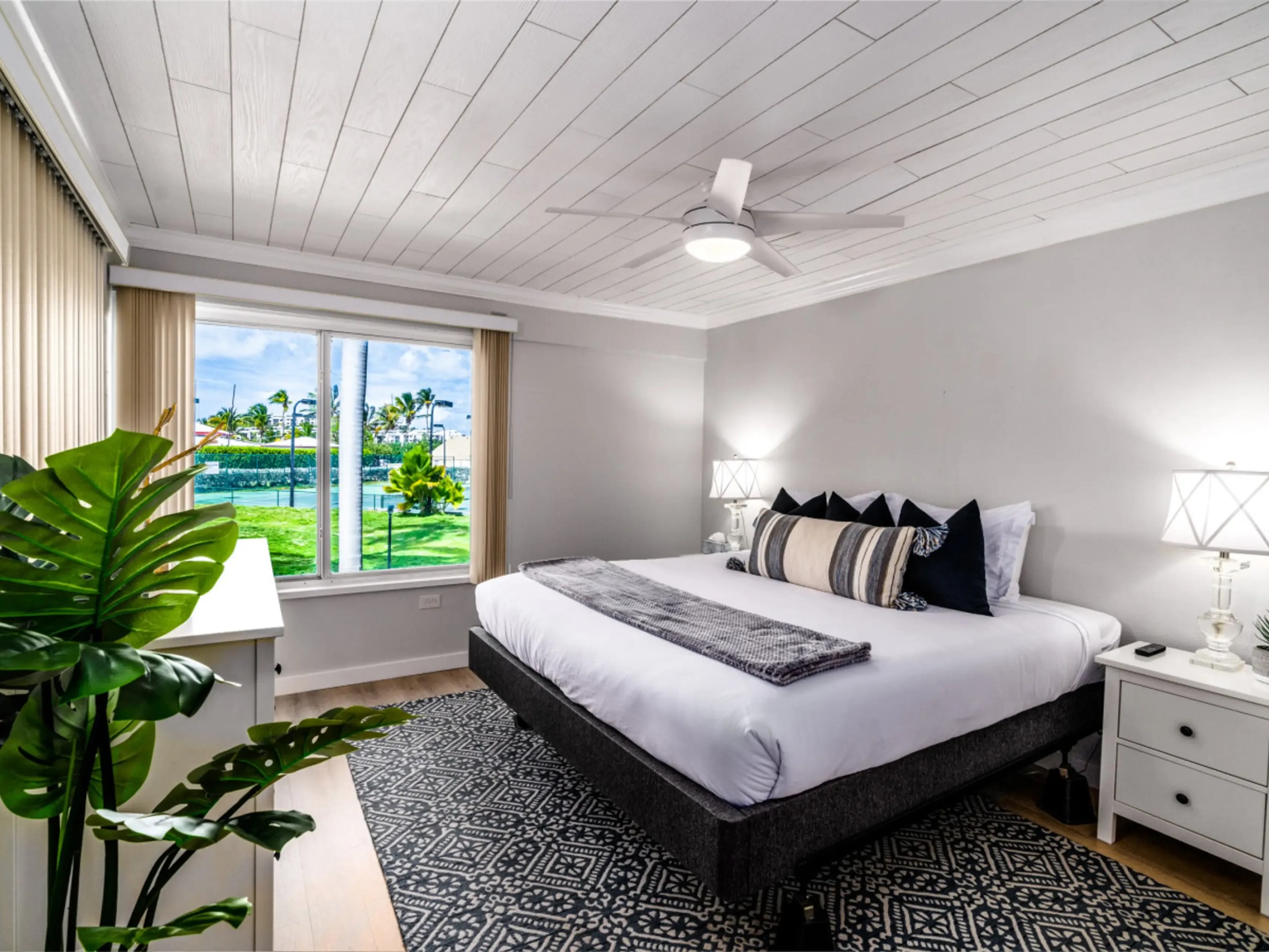 Bright bedroom with a large bed, lamps, and a window view of palm trees.