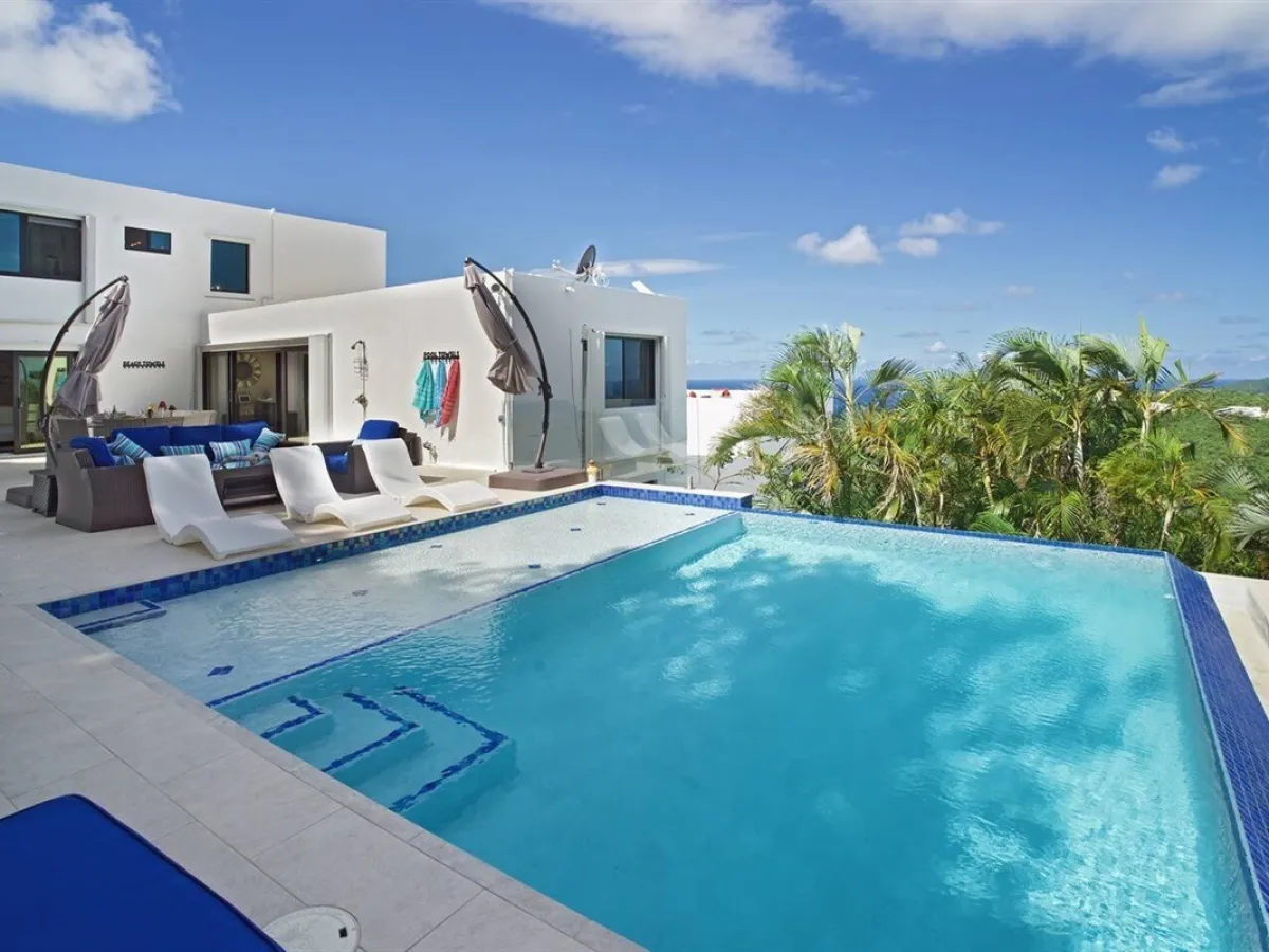 Modern villa with large pool, sun loungers, and ocean view under a clear blue sky.