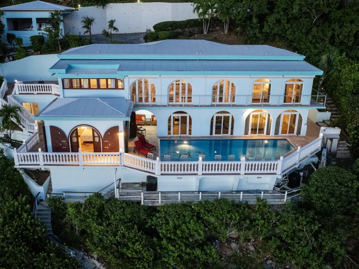 Two-story villa with large windows, balcony, and pool, surrounded by trees.