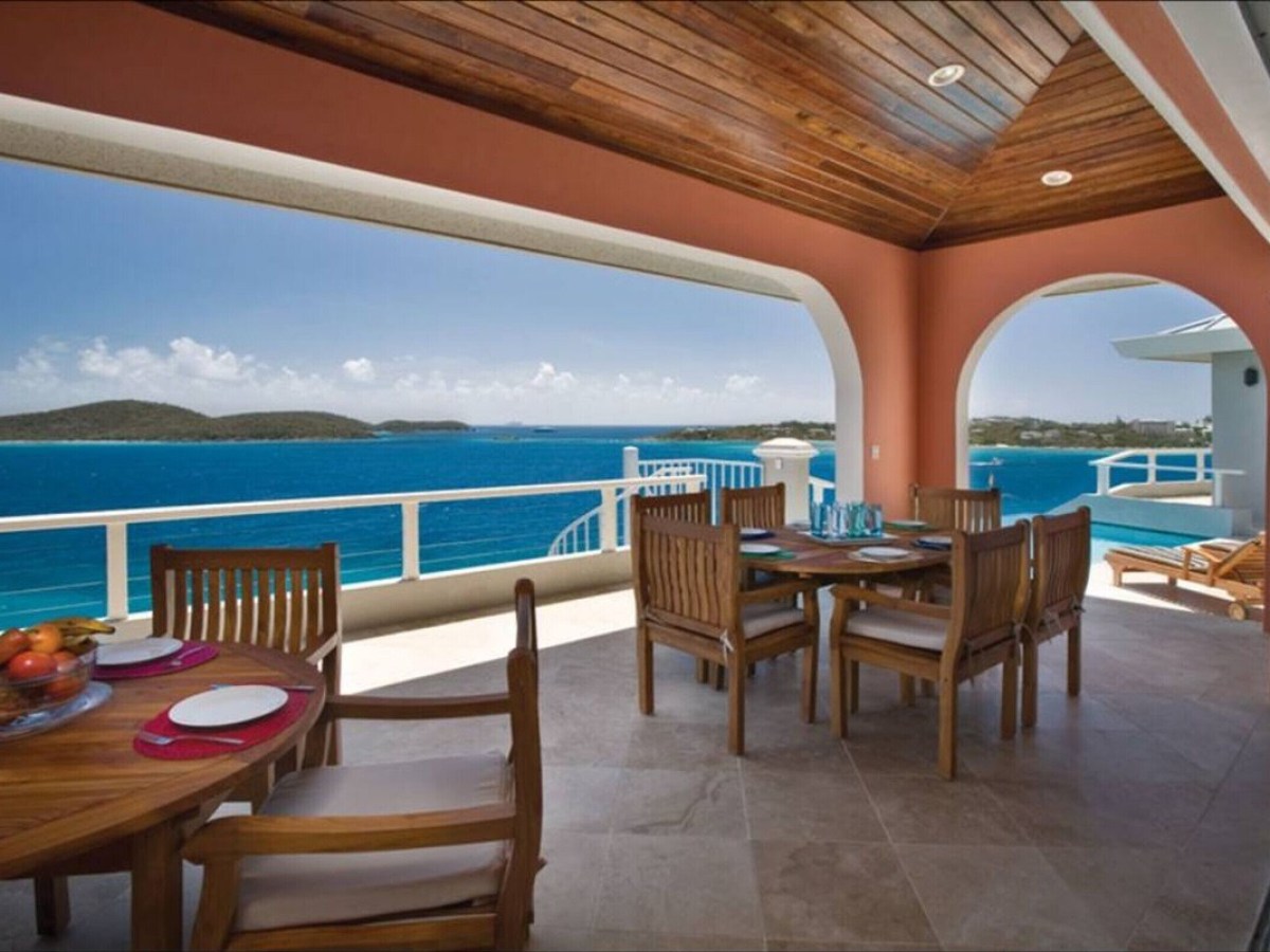 Covered patio with wooden tables and chairs overlooking the ocean and islands.