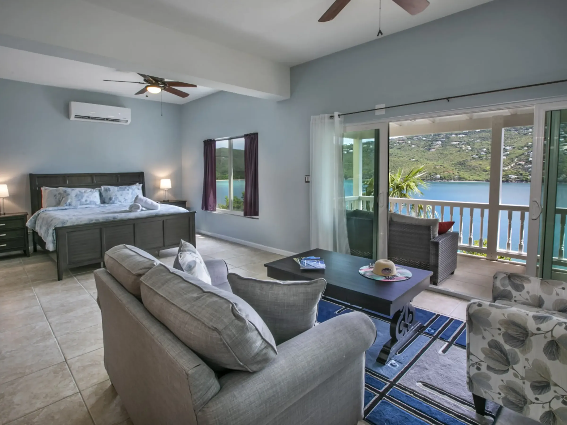 Spacious bedroom with a bed, sofa, and lake view through large sliding doors.