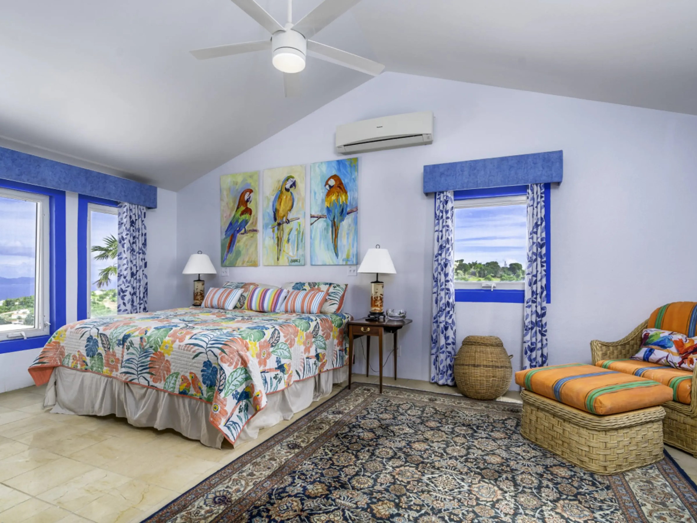 Colorful bedroom with parrot artwork, floral bedding, wicker chair, and blue curtains.