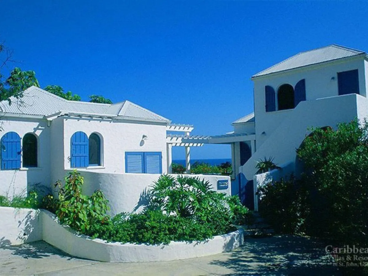 White villa with blue shutters, tropical plants, under clear blue sky.