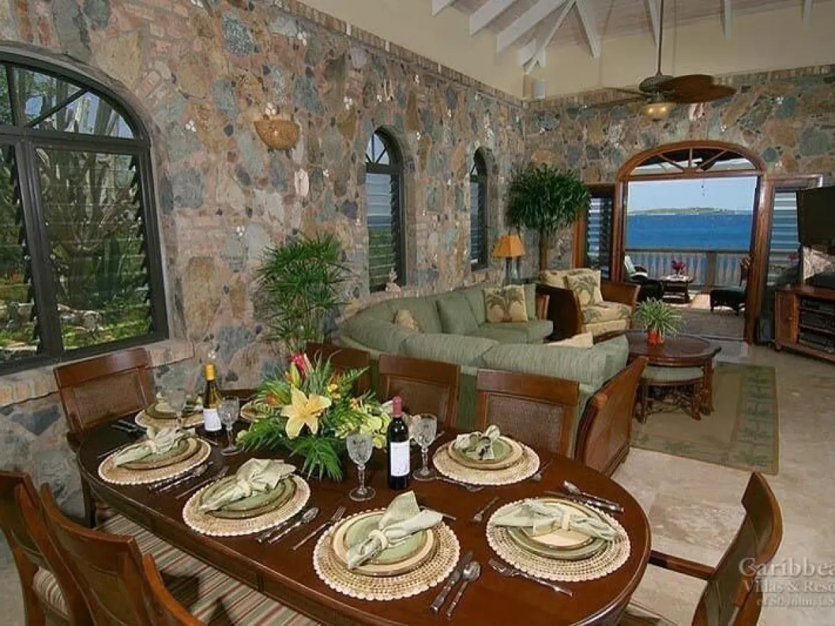 Elegant dining and living area with ocean view, set table, stone walls, and green couches.