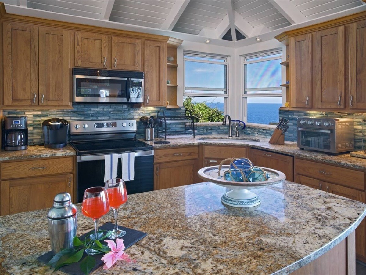 Modern kitchen with ocean view, wooden cabinets, granite counters, and decorative items on island.