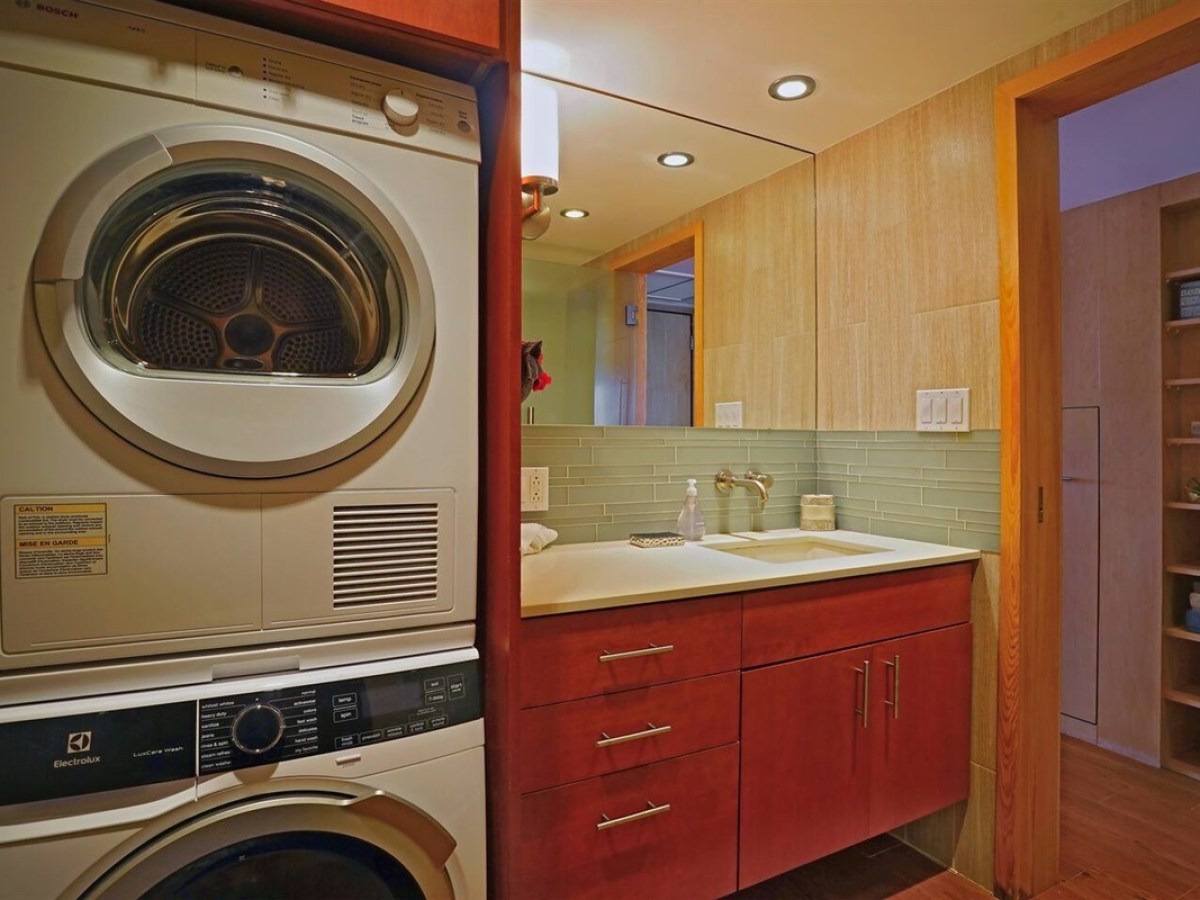 Laundry machines beside a bathroom sink with a mirror and wooden cabinetry.