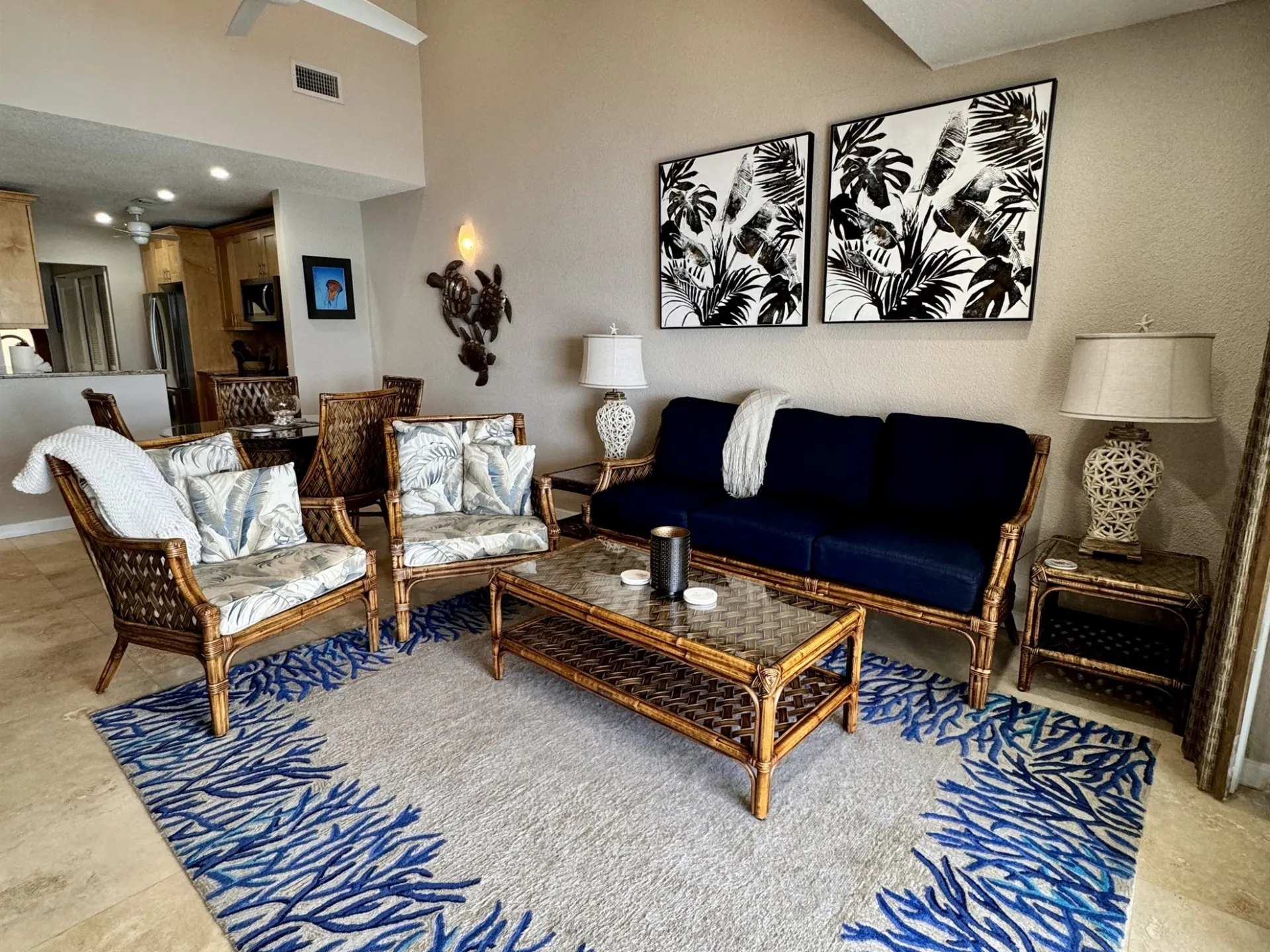 Coastal-themed living room with rattan furniture, blue sofa, palm artwork, and blue coral-patterned rug.