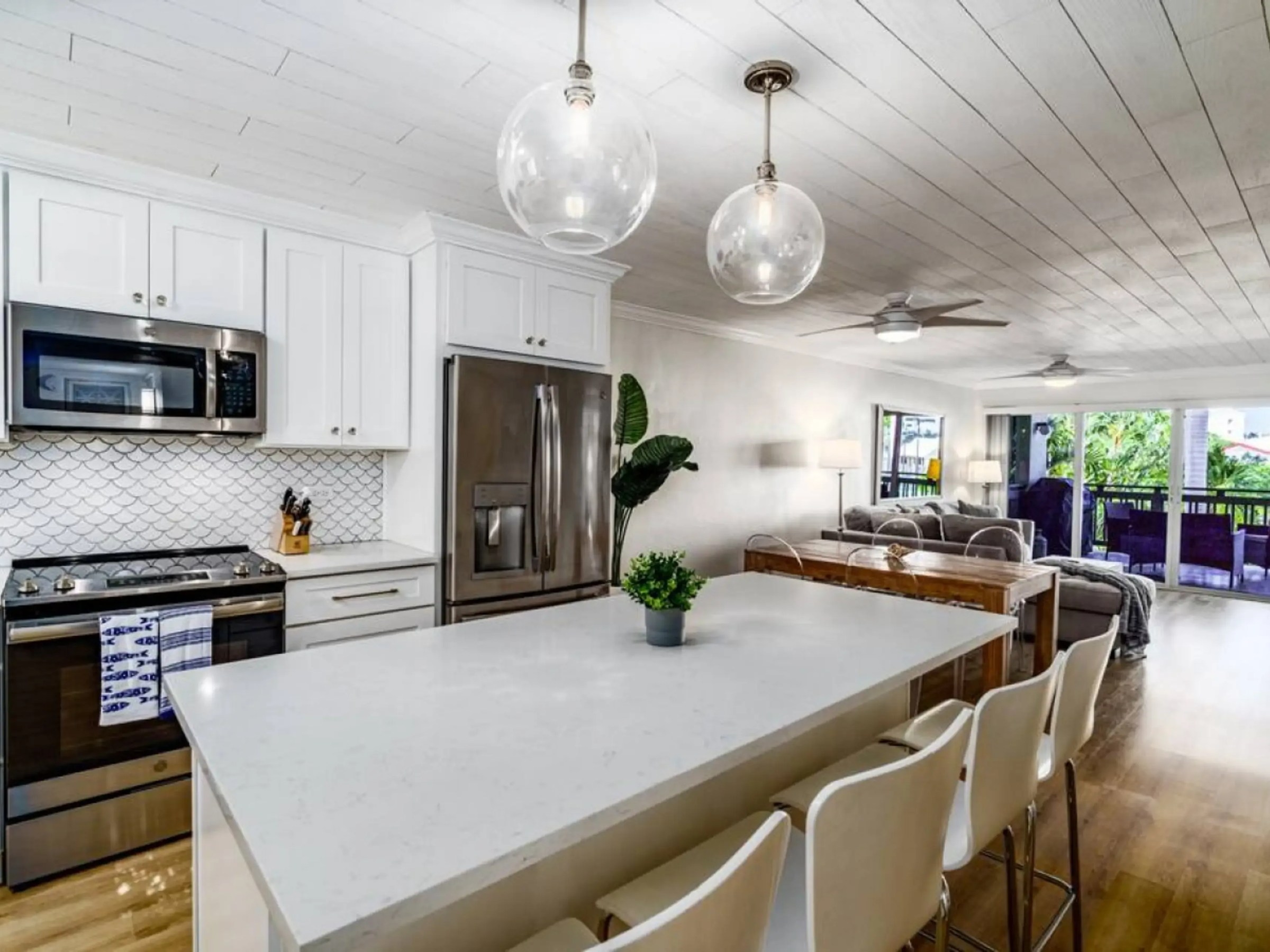 Modern kitchen and living area with white cabinets, large island, pendant lights, and balcony view.