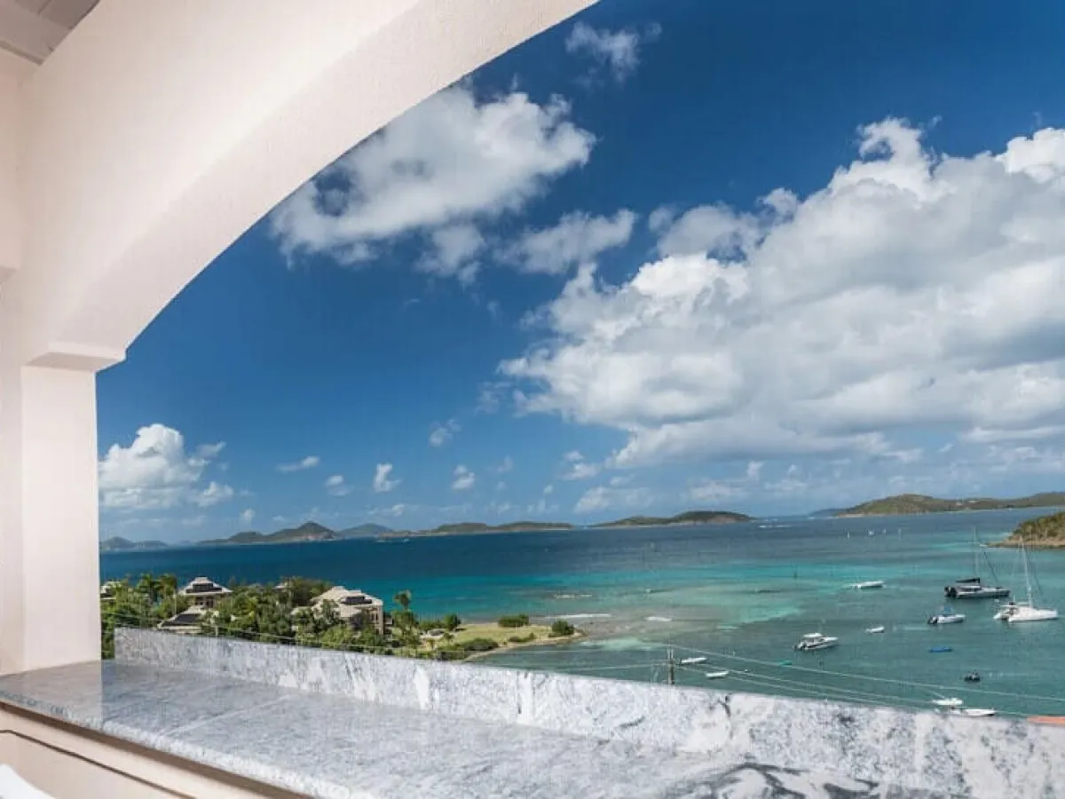 View of ocean with boats from a balcony under a cloudy sky.