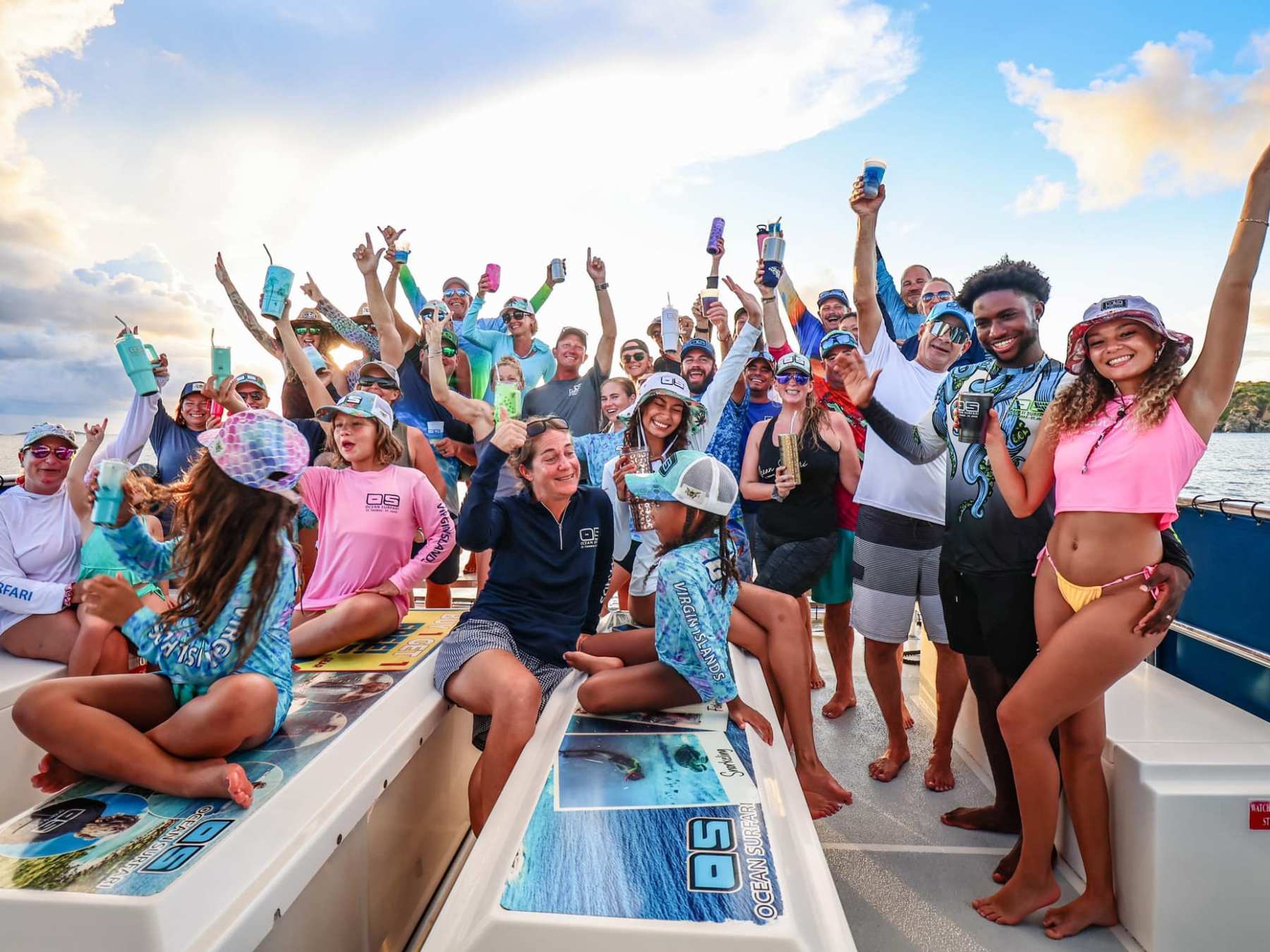 Group of people on a boat cheering with drinks and smiling at sunset.