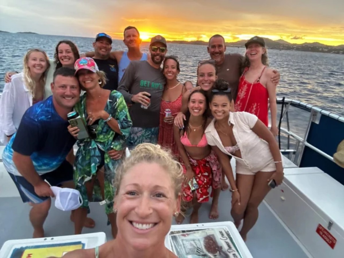 Group of people smiling on a boat at sunset, with ocean in the background.