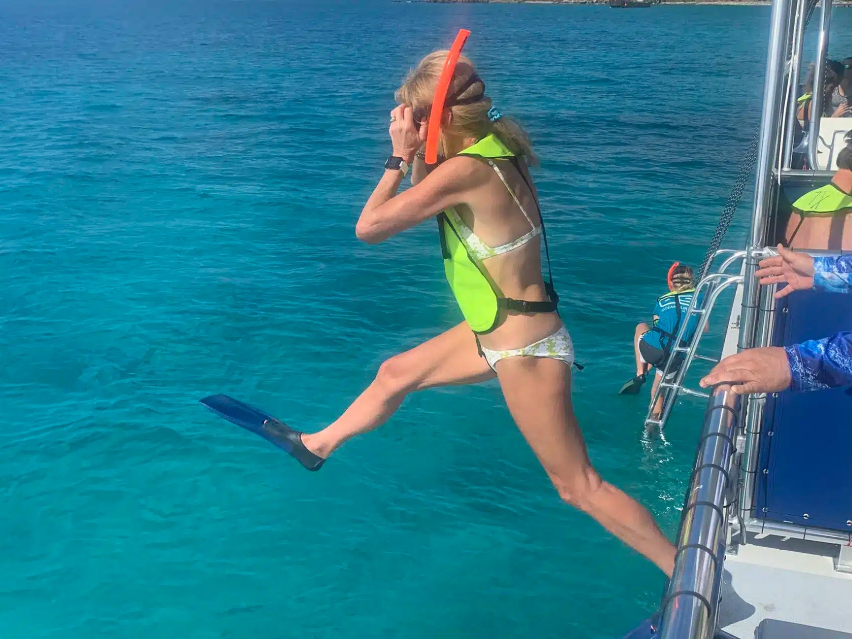 Person wearing snorkel gear and flippers jumps off boat into blue water.